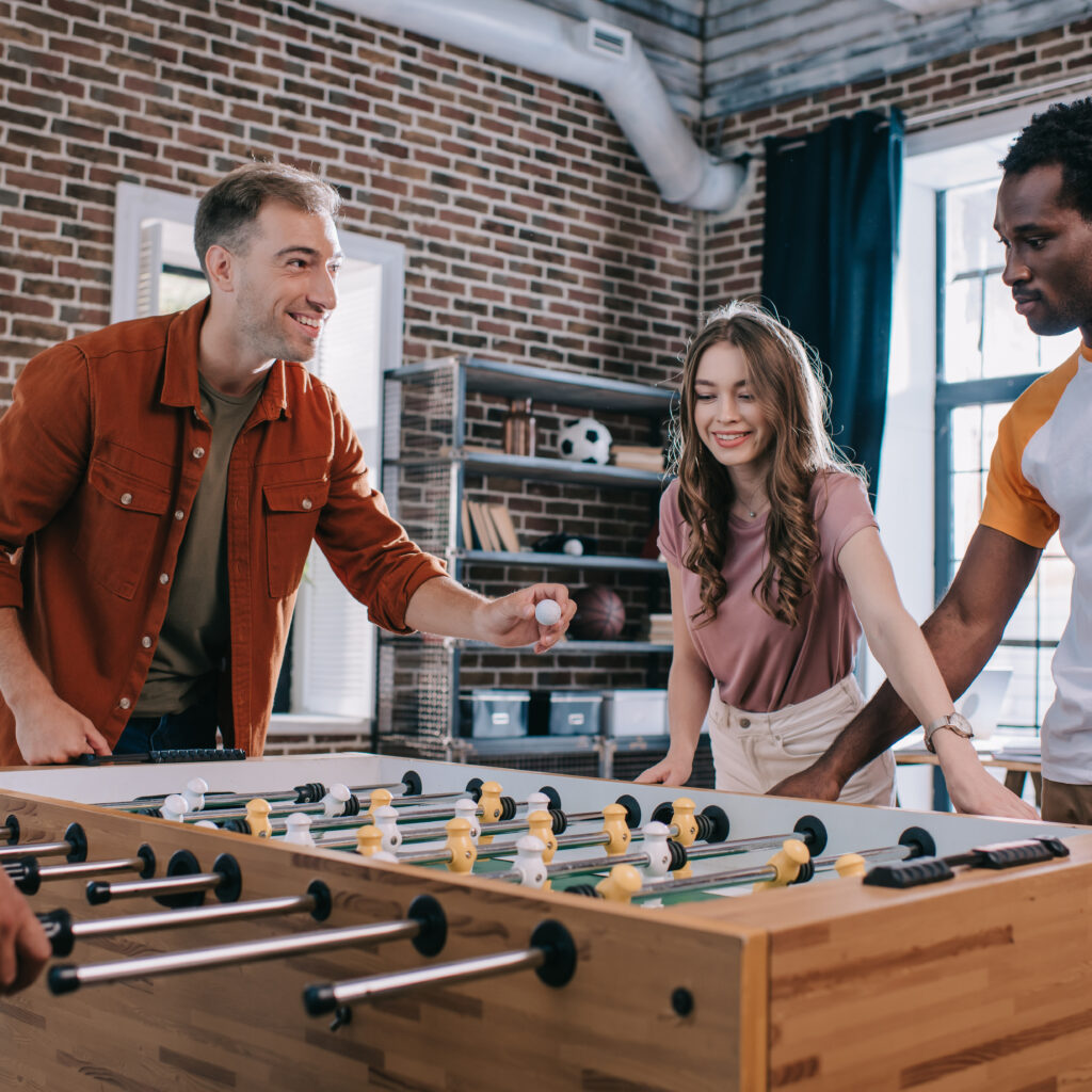 cheerful multicultural businesspeople playing table soccer in office