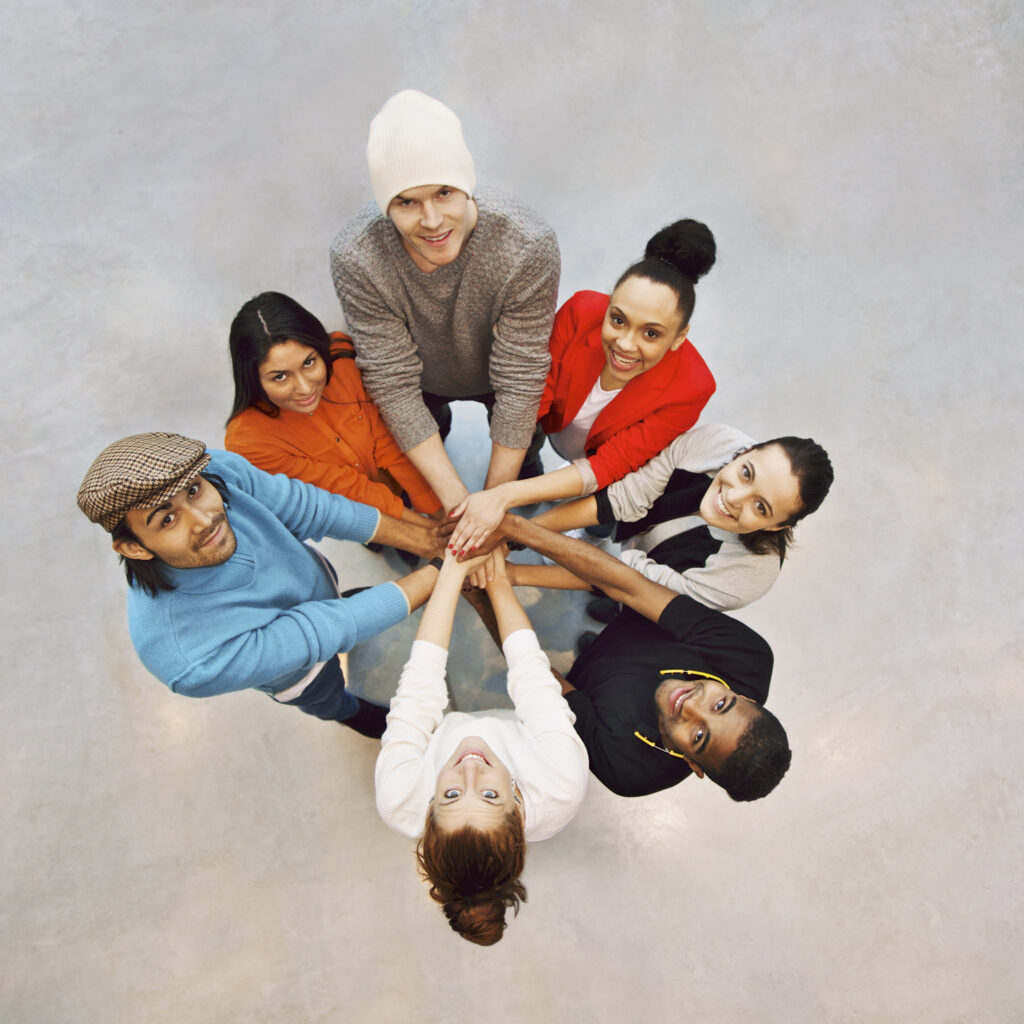 Group of happy young students showing. Top view of multiethnic group of young people putting their hands together. Young students standing in a circle making stack of hands showing unity as a team.